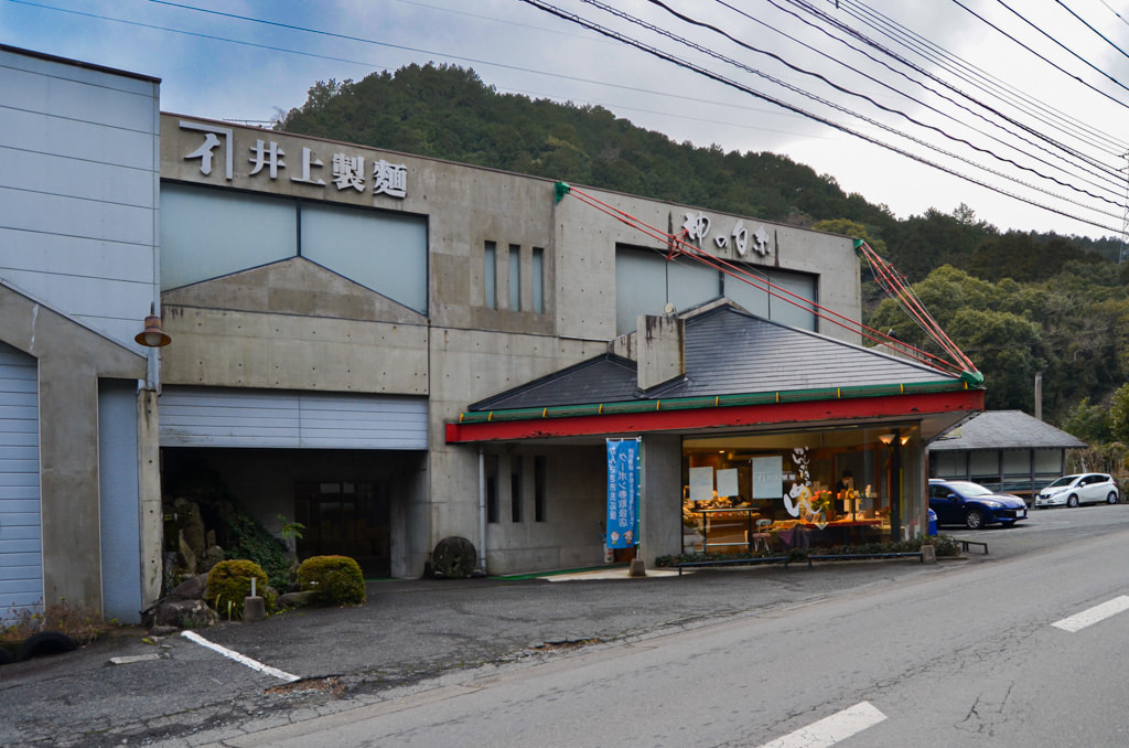 佐賀県神崎市の山あいにたたずむ井上製麺の社屋。近隣には美しい紅葉で知られる国の 名勝「九年庵」があり、入口付近に据えられた水車は脊振山系の清流を連想させる。